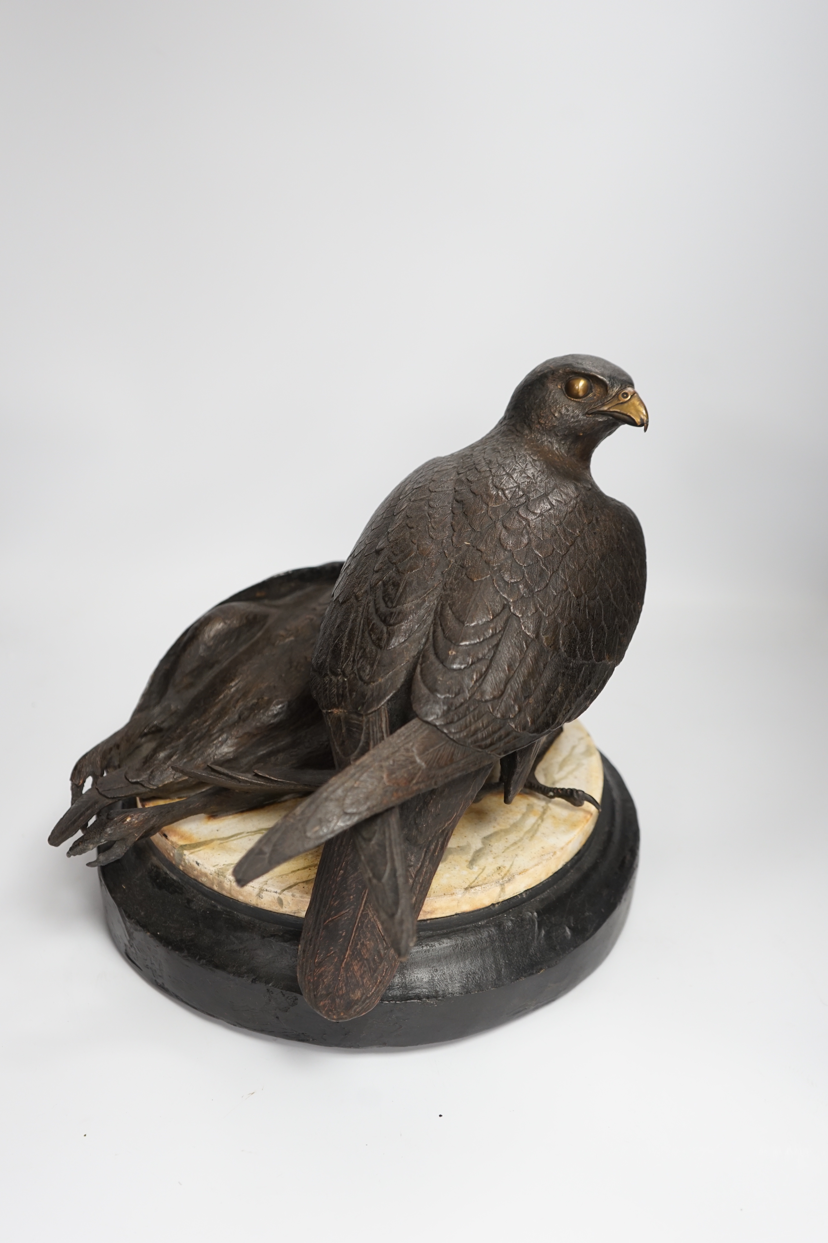 A limited edition bronze bird of prey with a kill, on a faux marble disc and painted wooden stand, 29cm high